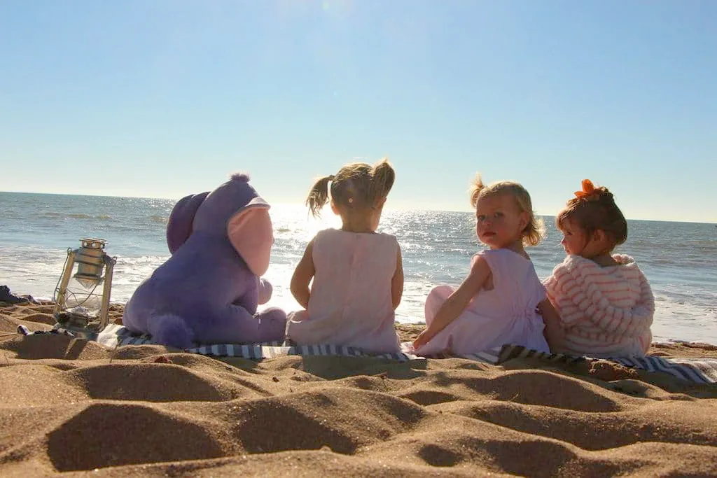 trois enfants assis sur la plage avec une peluche à côté