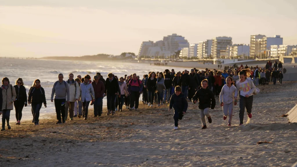 Groupe de personnes marchant sur la plage au coucher du soleil pendant l'événement La Dunaire Montoise