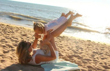 une maman fait faire l'avion à sa fille sur la plage