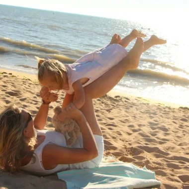 une maman fait faire l'avion à sa fille sur la plage