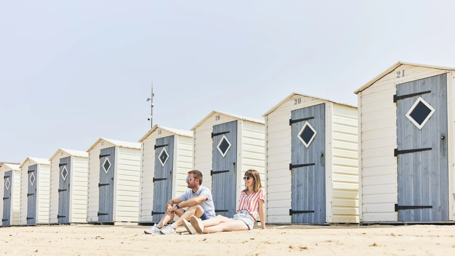 photo d'un couple assis sur la plage devant les cabines de notre dame de monts
