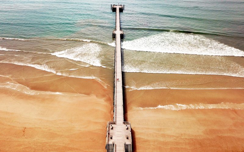 Photo en drone de l'estacade de Saint Jean de Monts. Le sable est orange et il y a des vagues qui donnent du mouvement à la mer.