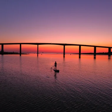 photo prise par un drone du pont de noirmoutier au coucher de soleil on y voit une personne sur un paddle dans la mer à Fromentine
