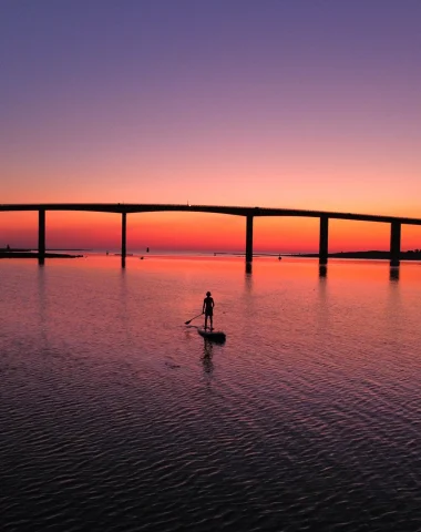 photo prise par un drone du pont de noirmoutier au coucher de soleil on y voit une personne sur un paddle dans la mer à Fromentine